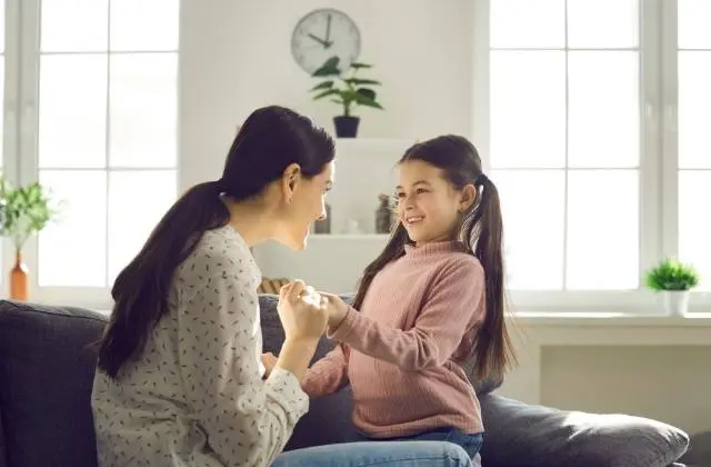 Adult and child smiling and holding hands on a sofa in a bright living room