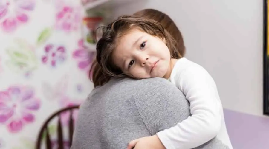 Child resting on an adult’s shoulder, seeking comfort indoors