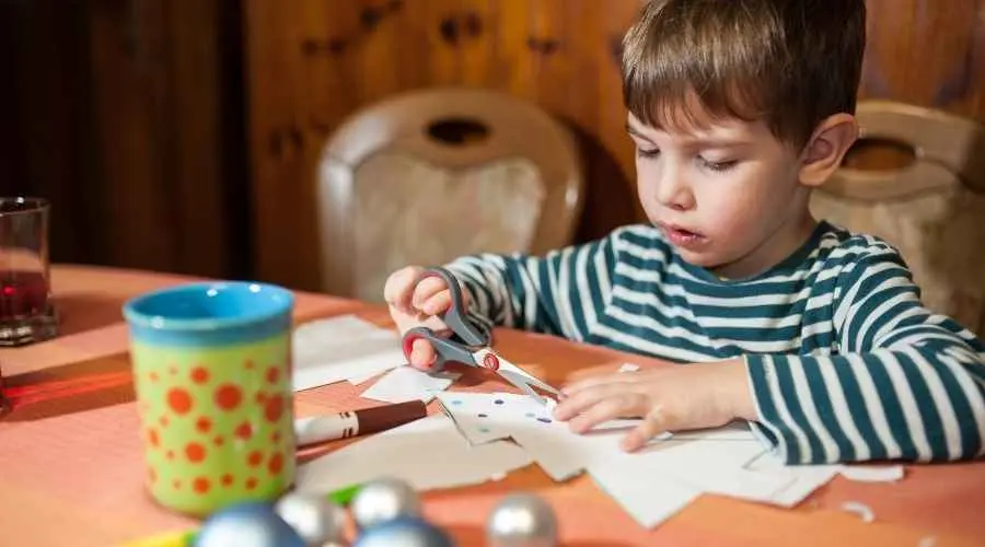 Child cutting paper with scissors at a table during a craft activity