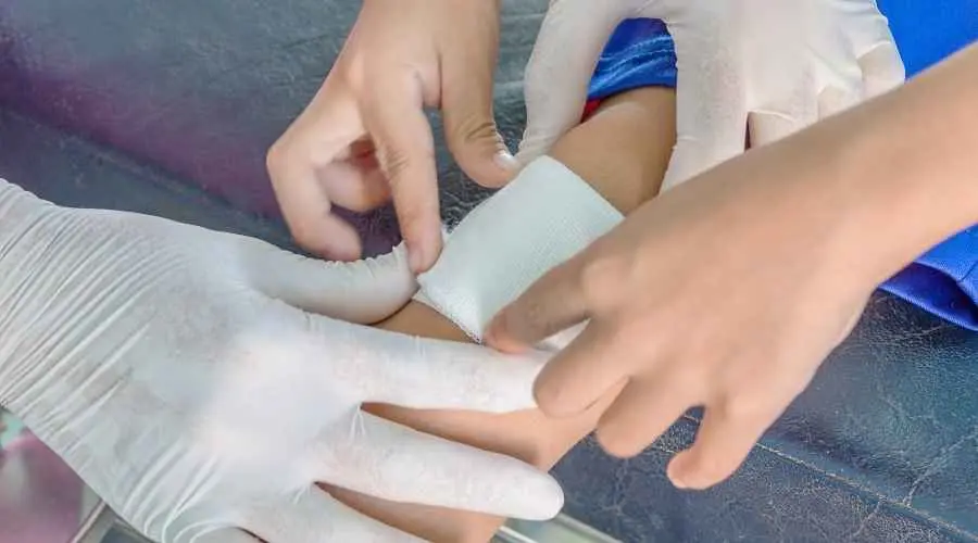 Gloved hands place a bandage on a child’s arm during medical care.