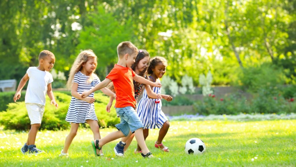 Children playing football together in a sunny park