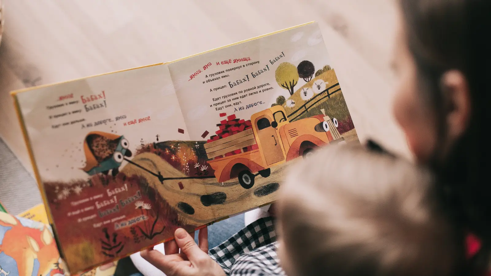 Adult and child look at a picture book showing a truck and printed text.
