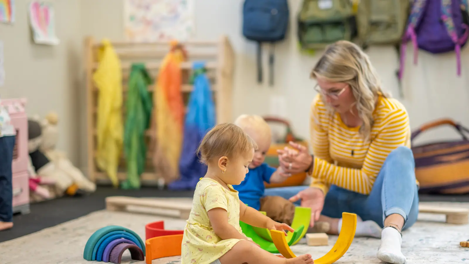 Adult with two infants playing with curved blocks in a nursery classroom.