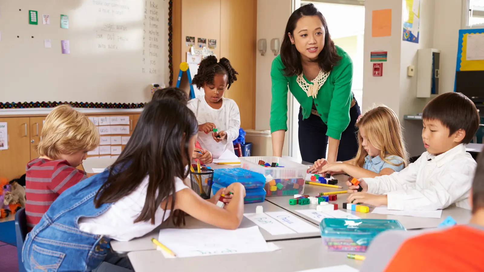Adult guides children using blocks at a classroom table.