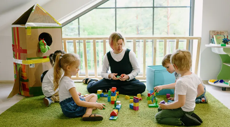 Adult and children building with blocks on a carpet in a bright playroom