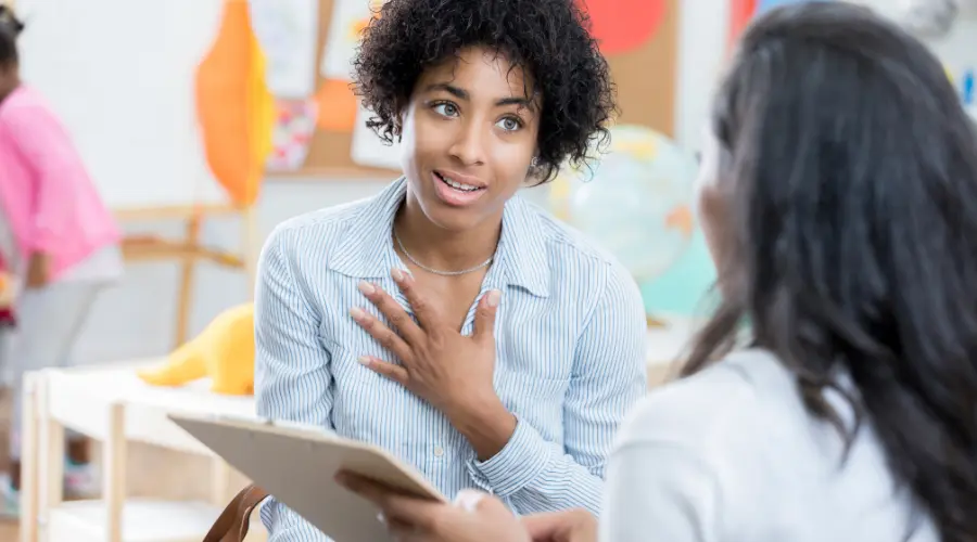 Adult speaking to another adult in a classroom, holding a tablet