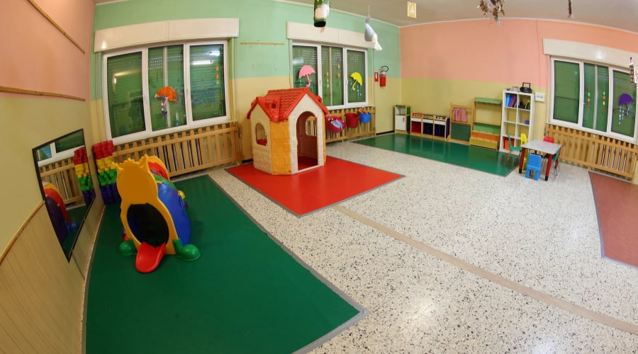 Empty nursery playroom with a toy house, slide, shelves and small table.