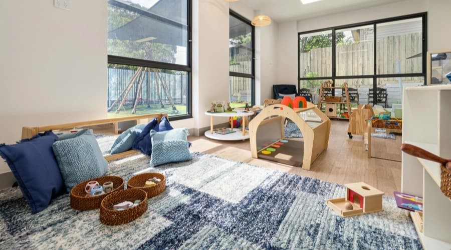 Bright empty nursery room with rugs, cushions, wooden toys and large windows.